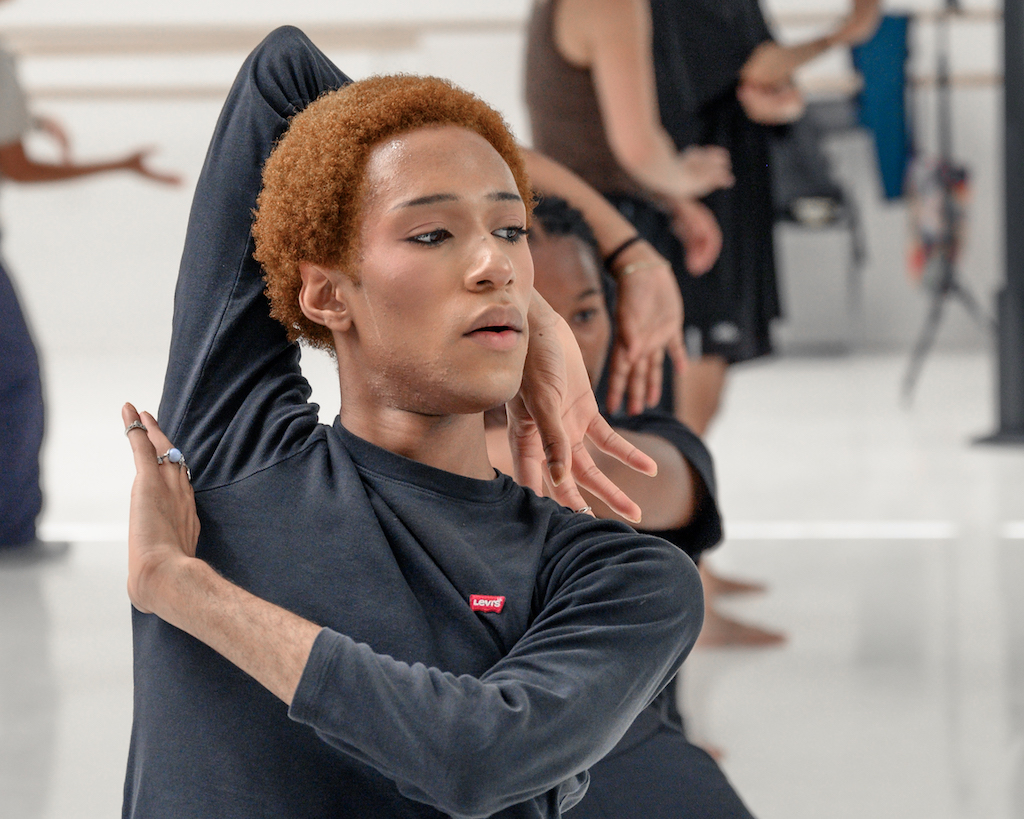 Dancers pose and wrap their arms around their heads in mid-studio practice